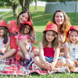 Friends enjoying a sunny day picnic on grass with bucket hats and smiles in a Portuguese park.