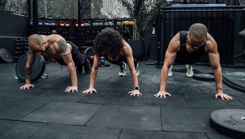 Three individuals performing push-ups together in a Mexico City gym setting.